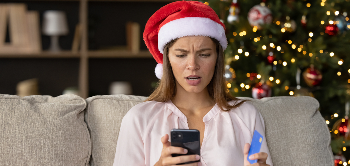 Junge Frau vor Christbaum schaut besorgt auf ihr Mobiltelefon